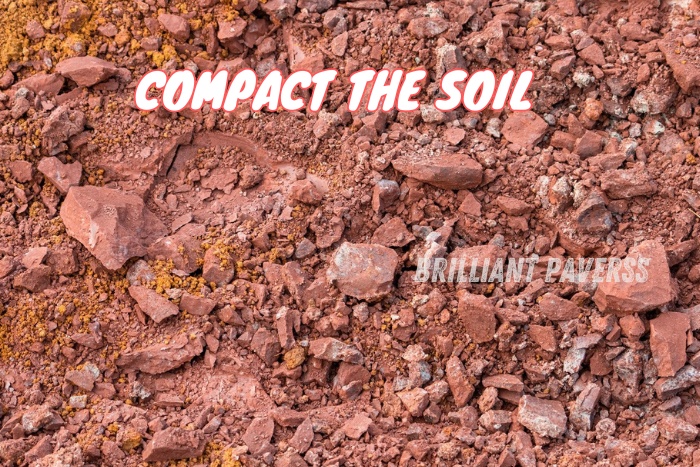 Close-up of soil ready for compaction with the text "COMPACT THE SOIL" and the Brilliant Paverss logo, highlighting the essential step of soil preparation for high-quality paver installations by Brilliant Paverss in Coimbatore.